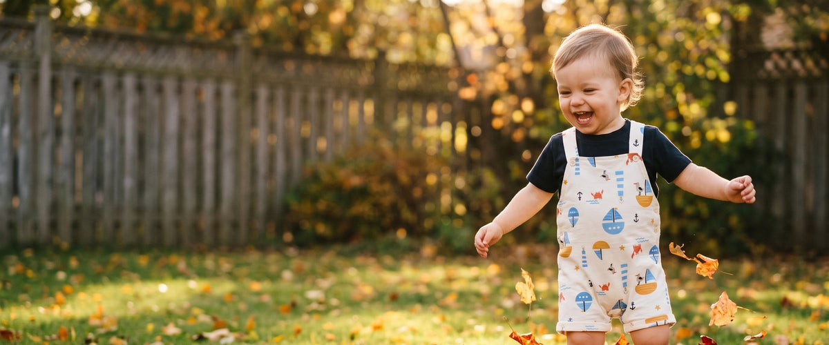 Toddler in cotton overalls running through autumn leaves