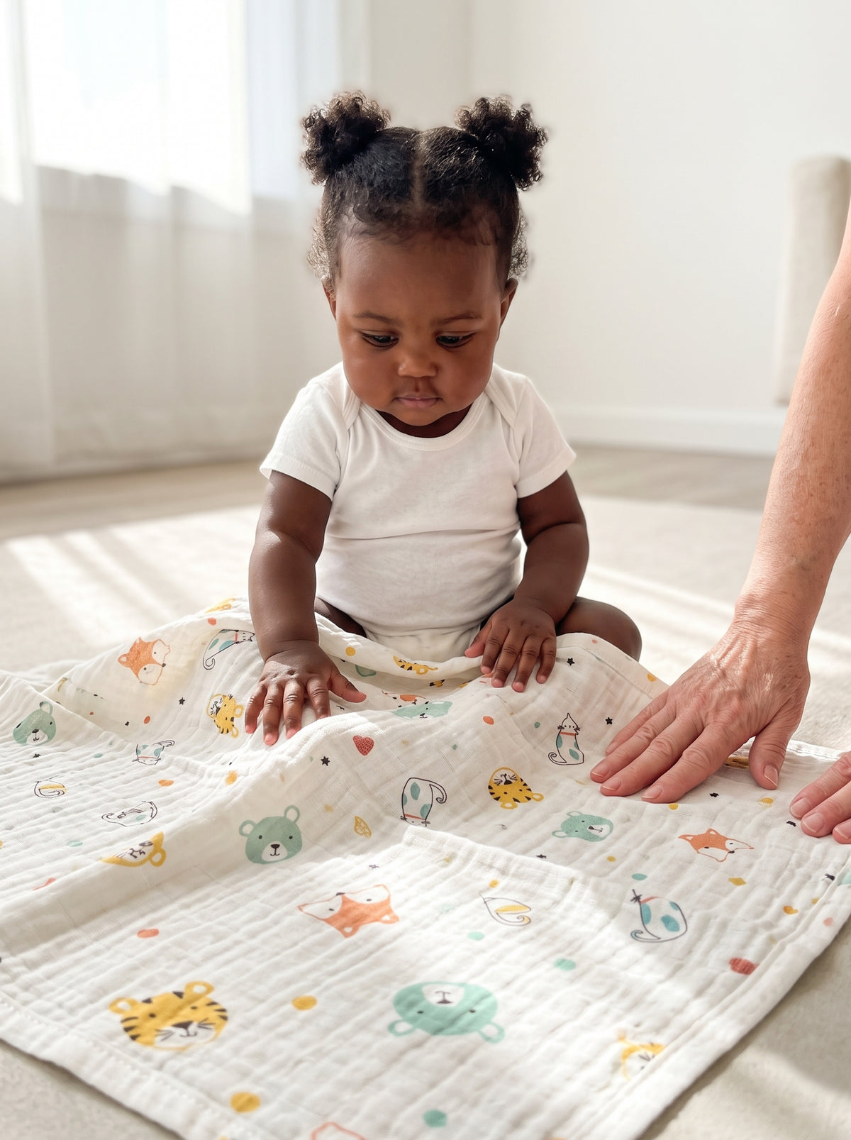 A nine-month-old baby girl sitting up on a large cream mulmul muslin cloth spread flat on the floor, an older adult's hand smoothing the edge beside her. AI-generated image.