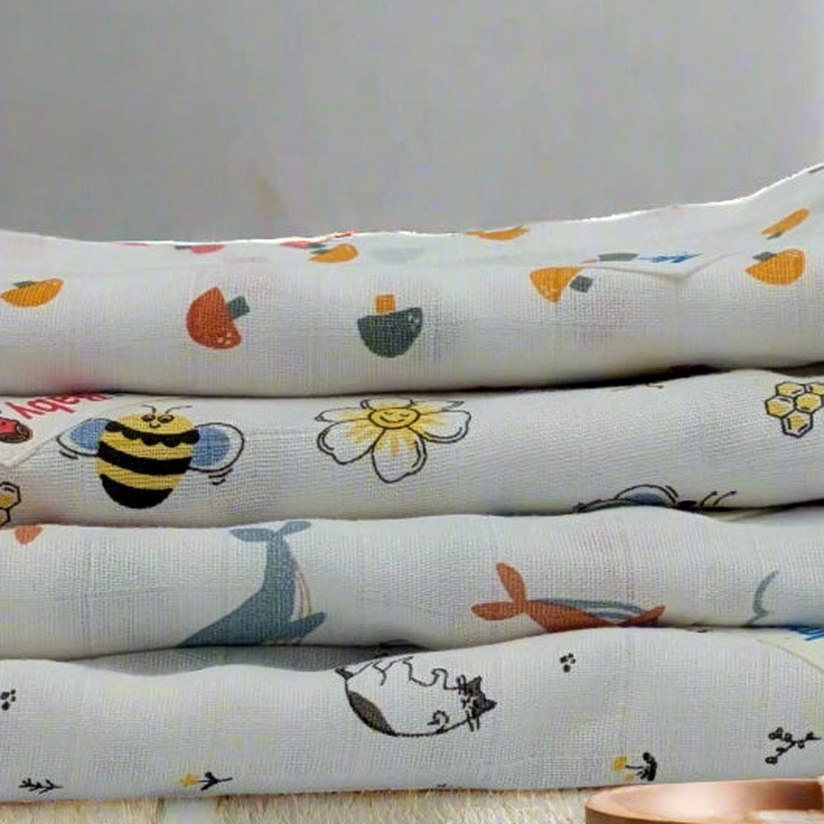 All four mulmul muslin baby towels laid out together, printed with shapes, bees, whales and cats.