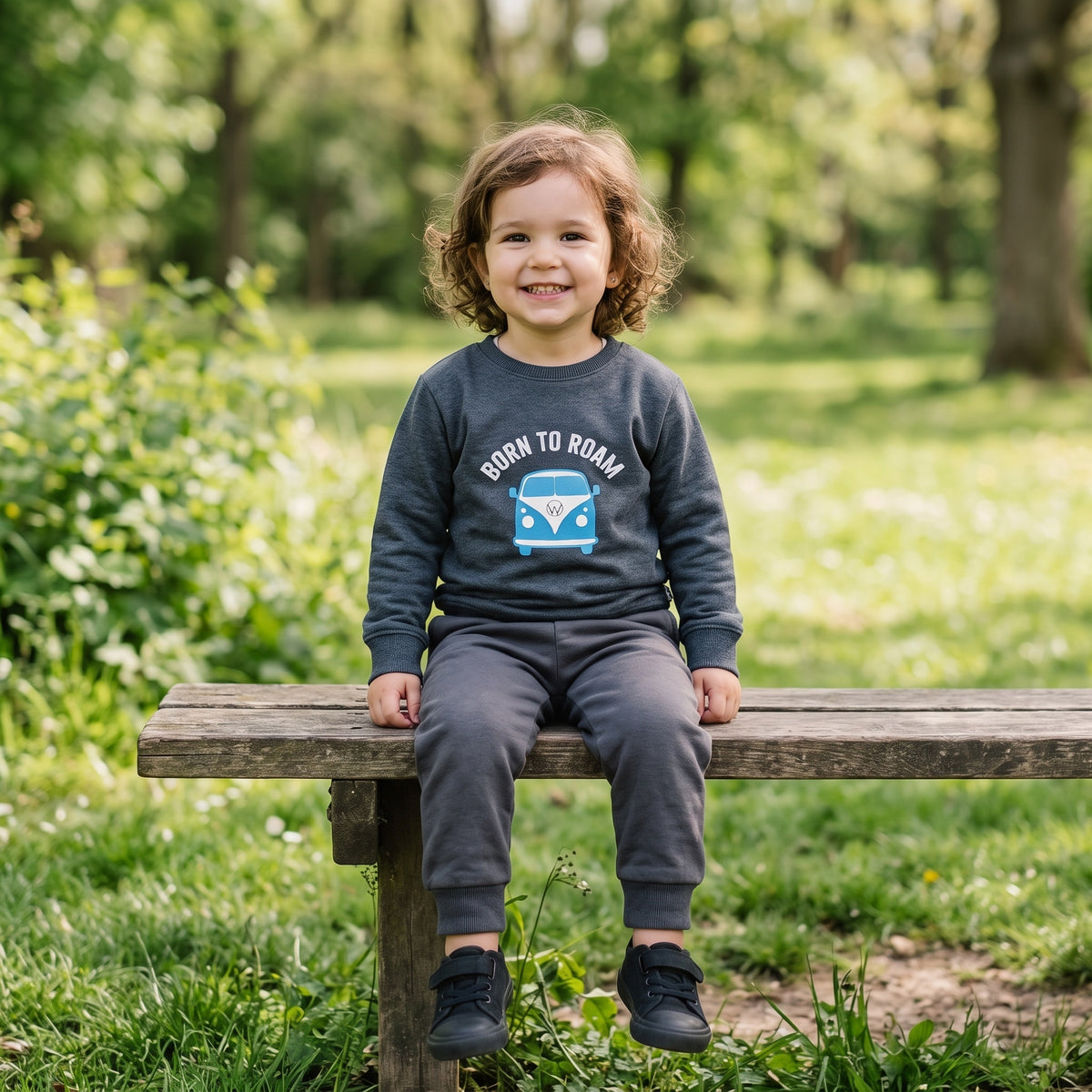 A three-year-old sitting on a park bench, wearing the charcoal Born to Roam cotton sweatshirt. AI-generated image.