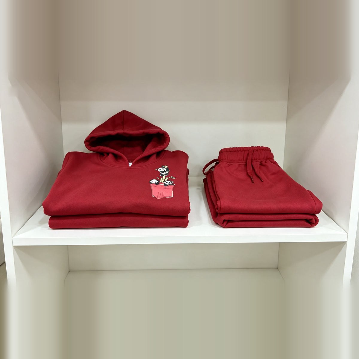 The red Panda Pocket cotton hoodie and matching joggers folded on a white shelf.