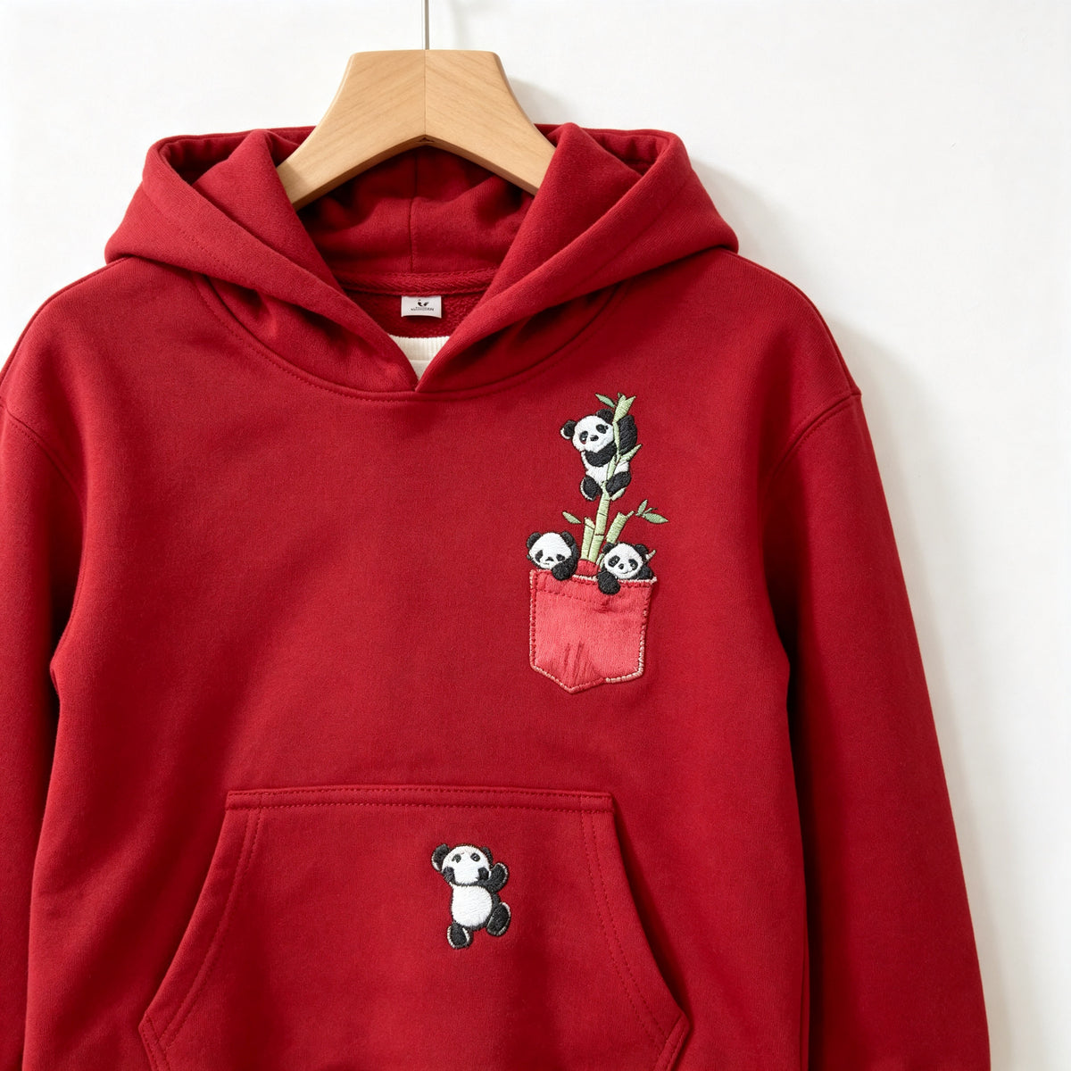 Close view of the red Panda Pocket cotton hoodie on a wooden hanger, showing the printed chest pocket with pandas and the sewn front pouch.