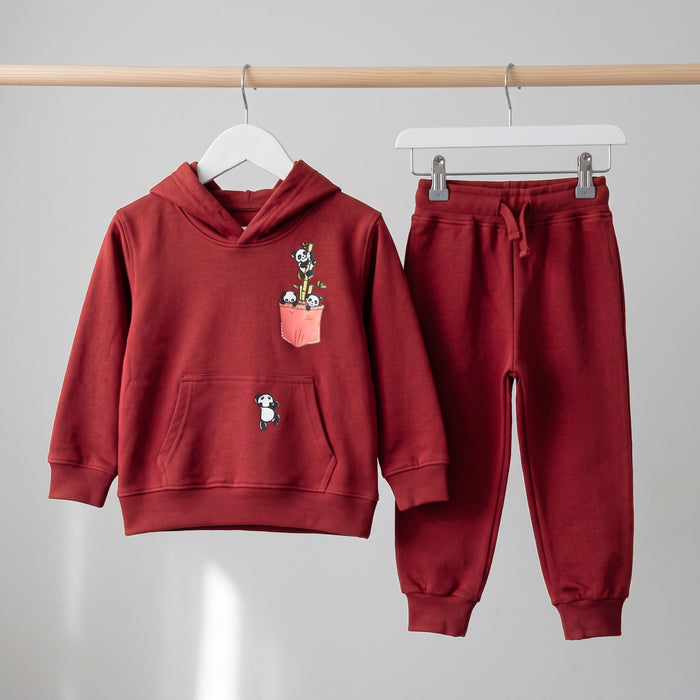 The red Panda Pocket cotton hoodie and matching joggers on hangers against a pale wall.