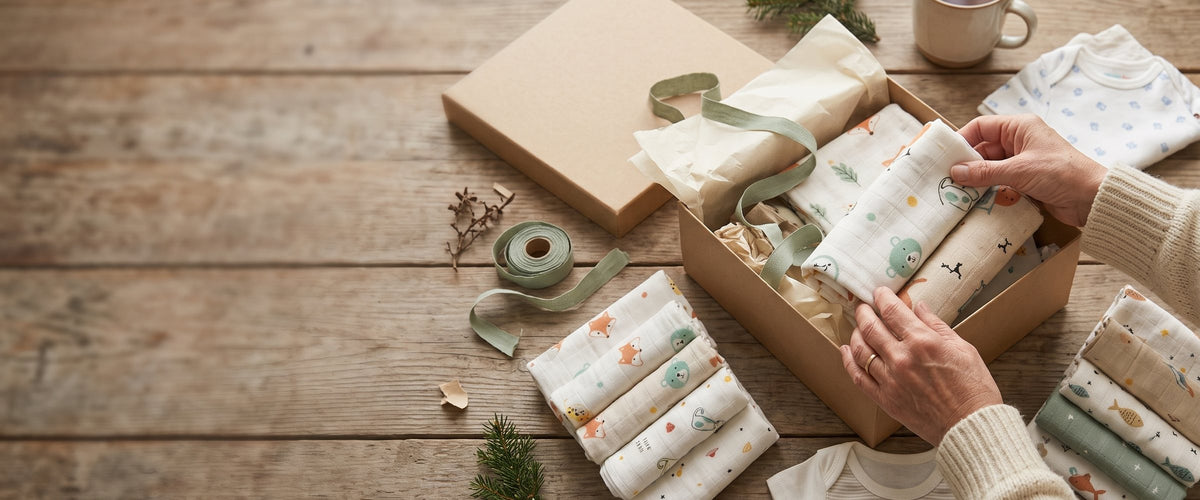 Hands packing a box of muslin baby gifts
