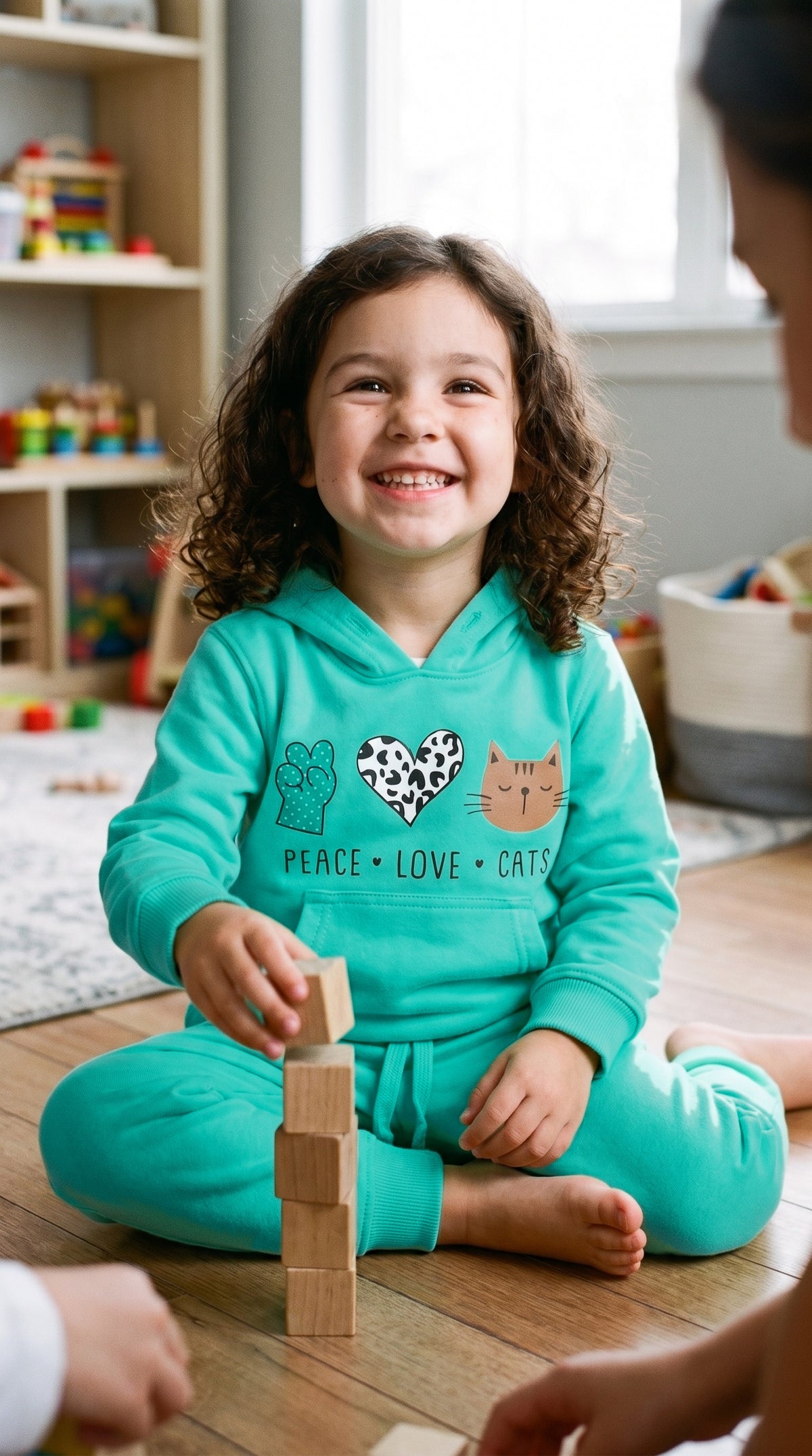 Child in the mint hoodie and jogger set building a wooden block tower