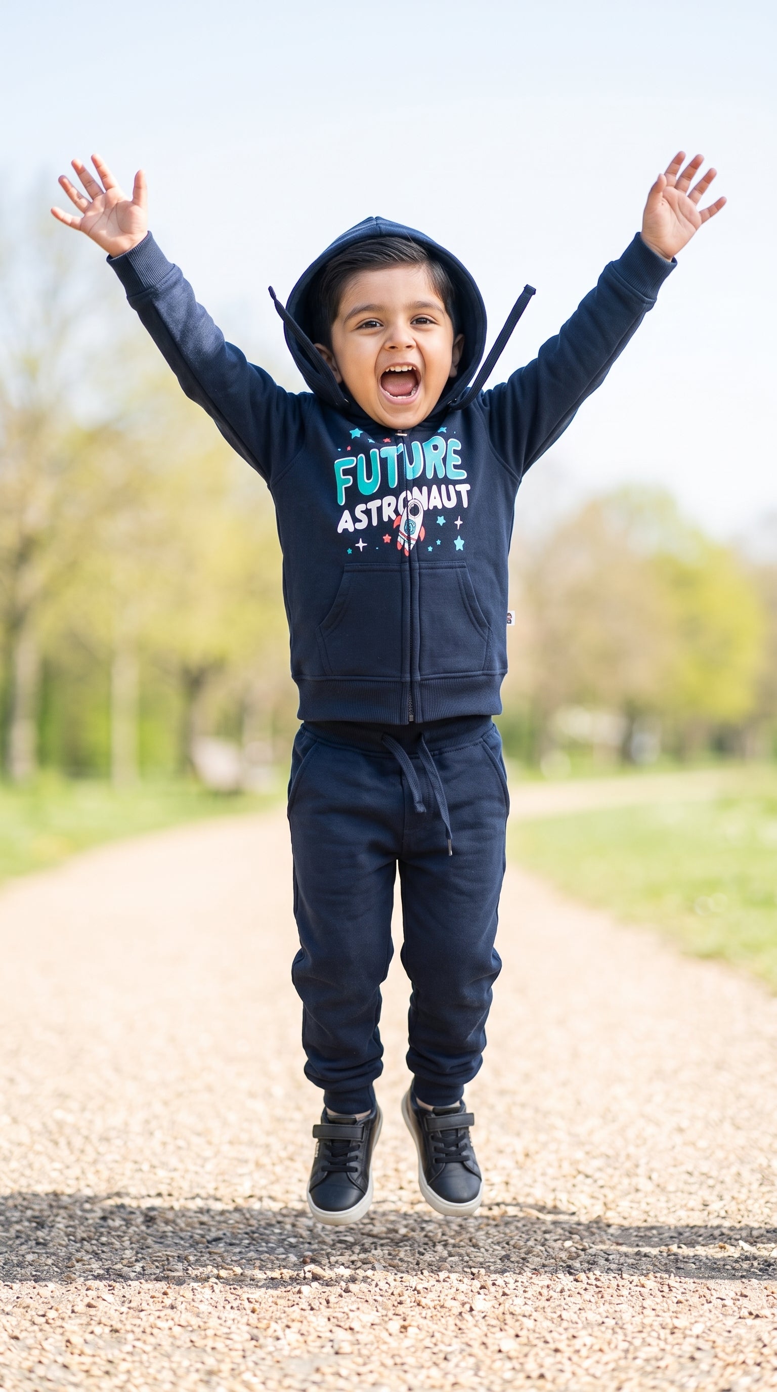 Boy jumping on a park path in the navy Future Astronaut zip hoodie and jogger set