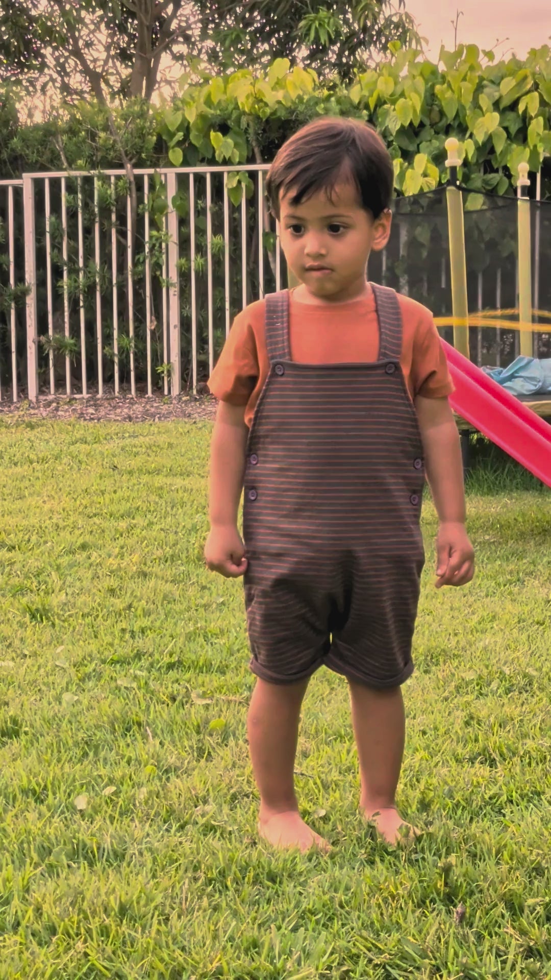Real toddler wearing the Burnt Orange Stripes muslin dungaree set in the backyard