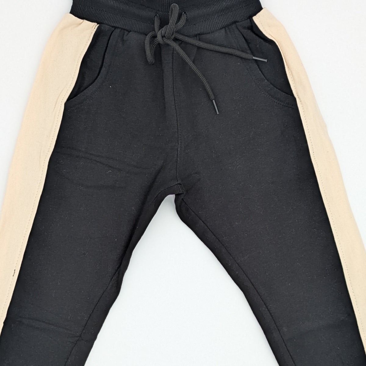 Close view of the black cotton joggers showing the cream side stripe, the ribbed drawstring waistband and the slant front pockets.