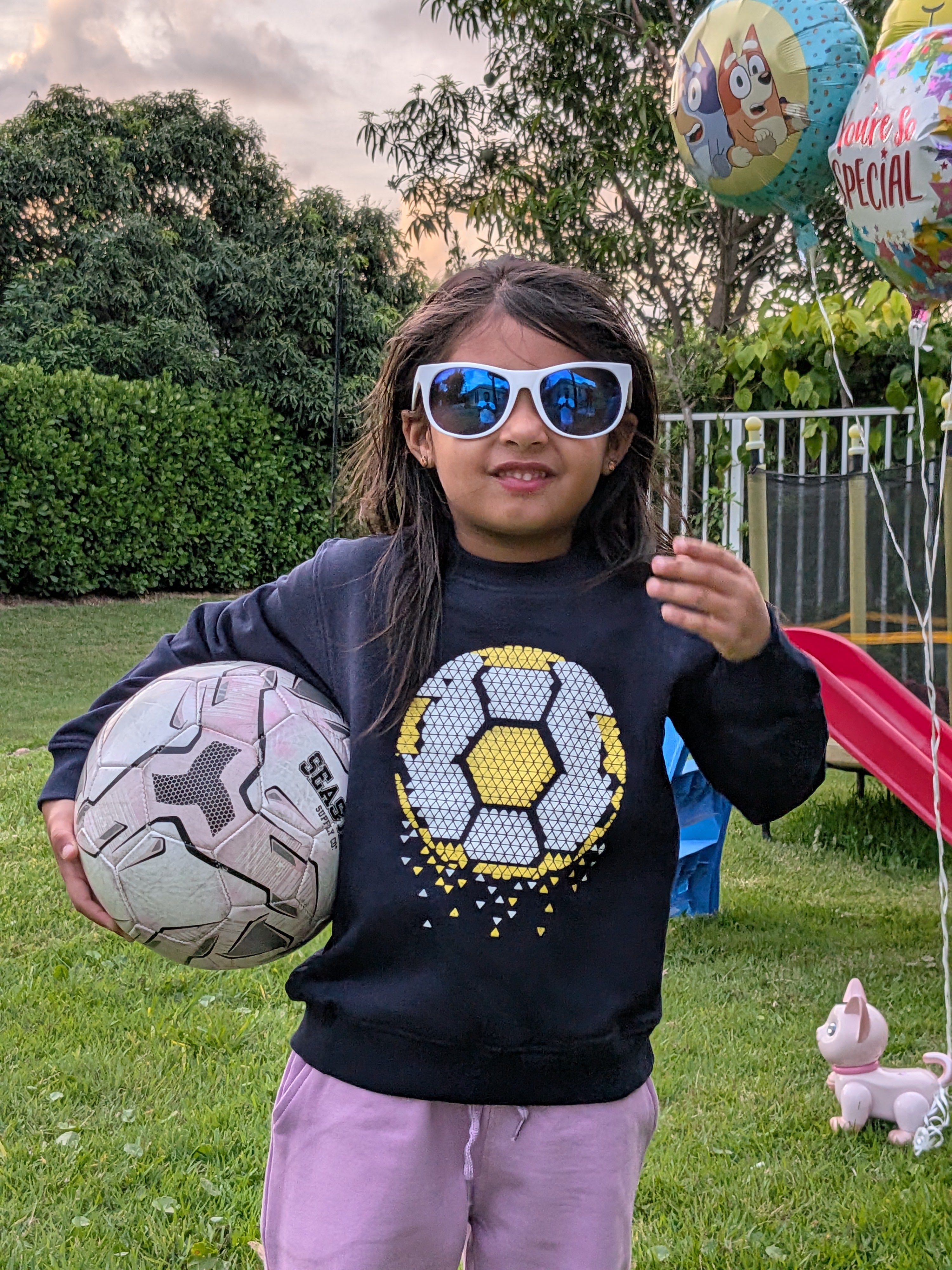 Child wearing MulmulBaby navy Soccer Time organic cotton sweatshirt, holding a soccer ball outdoors at sunset